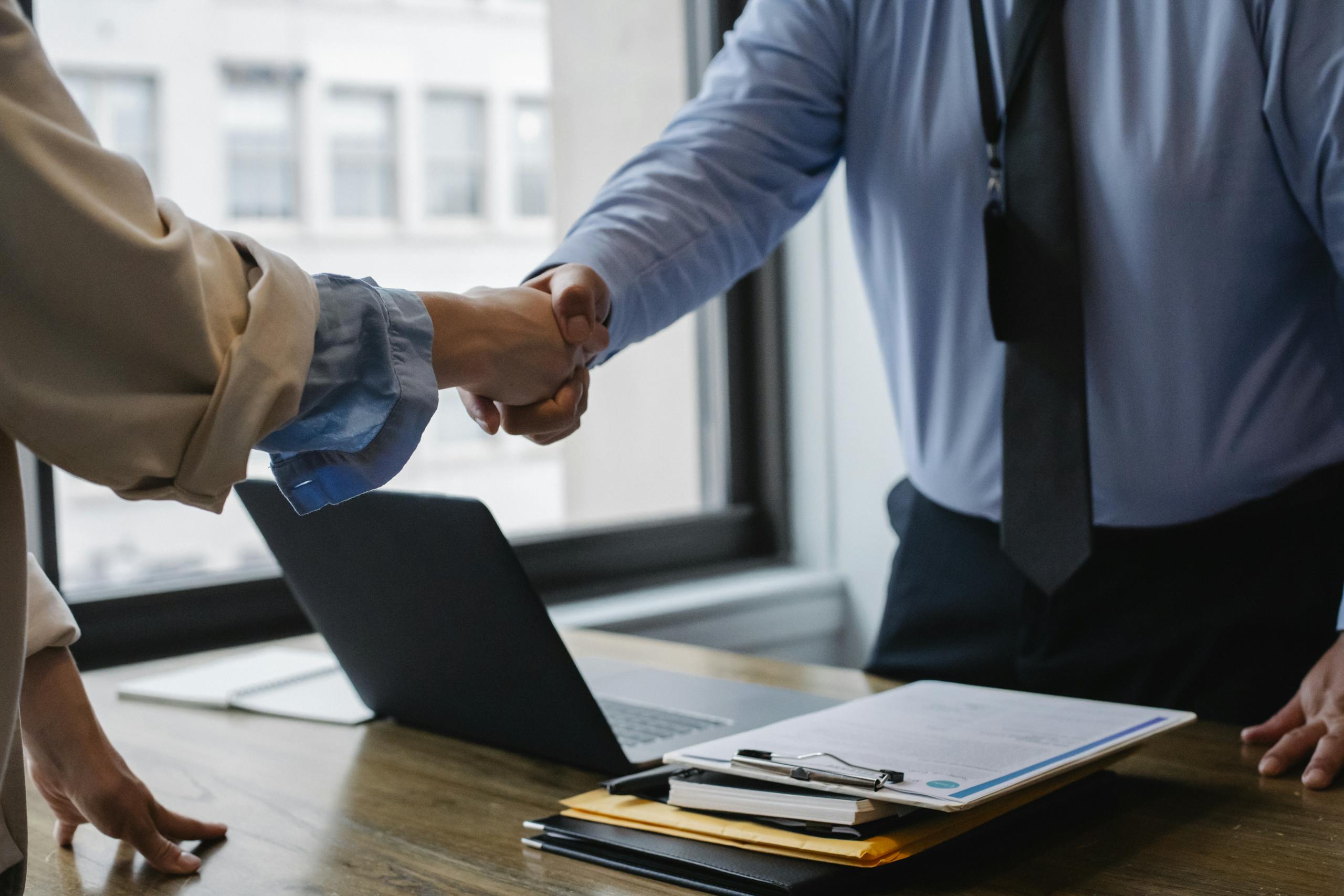 Coworkers standing at table with laptop and documents while greeting each other before meeting